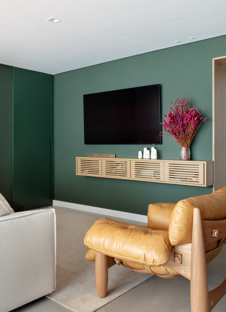 Sala de TV com parede verde profundo e poltrona Mole caramelo — projeto de interiores Obrafy no Brooklin